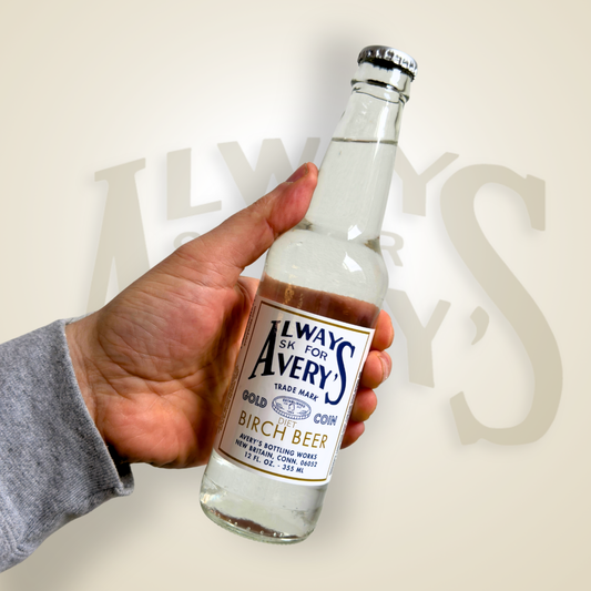 Hand holding a bottle of Avery’s Diet Birch Beer in glass bottle on beige gradient background