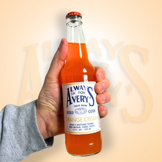 Hand holding a bottle of Avery’s Orange Cream Soda in glass bottle on orange gradient background