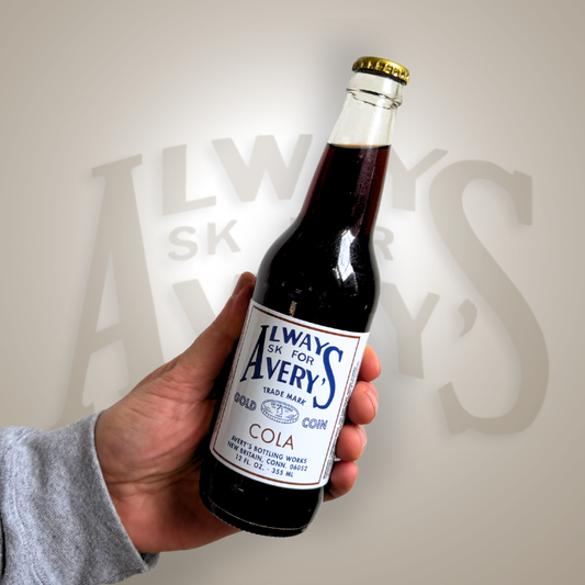 Hand holding a bottle of Avery’s Cola in glass bottle on brown gradient background