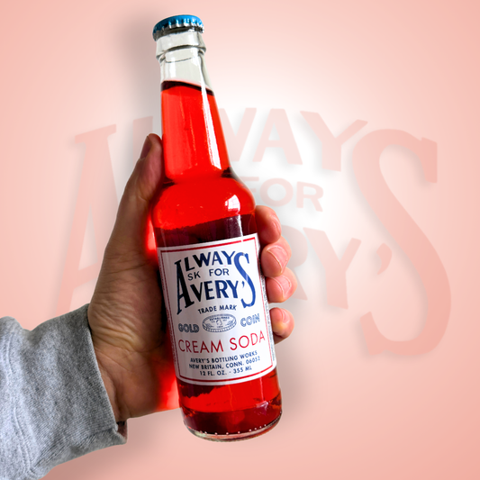 Hand holding a bottle of Avery’s Cream Soda in glass bottle on red gradient background