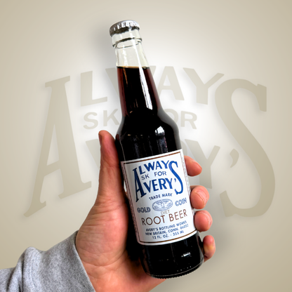 Hand holding a bottle of Avery’s Diet Root Beer in glass bottle on brown gradient background