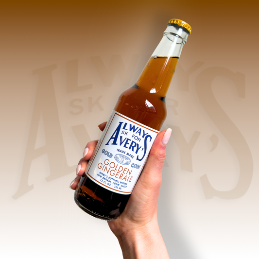 Hand holding a bottle of Avery’s Ginger Ale in glass bottle on golden gradient background