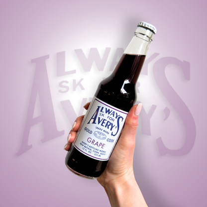 Hand holding a bottle of Avery’s Grape Soda in glass bottle on purple gradient background