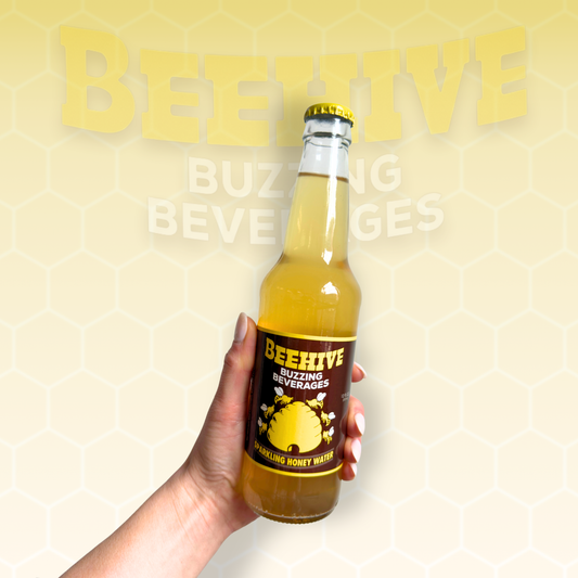 Hand holding a bottle of Avery’s Honey Infused Sparkling Honey Water in glass bottle on yellow gradient background