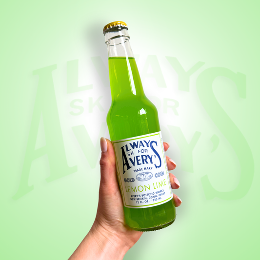 Hand holding a bottle of Avery’s Lemon Lime green Soda in glass bottle on green gradient background