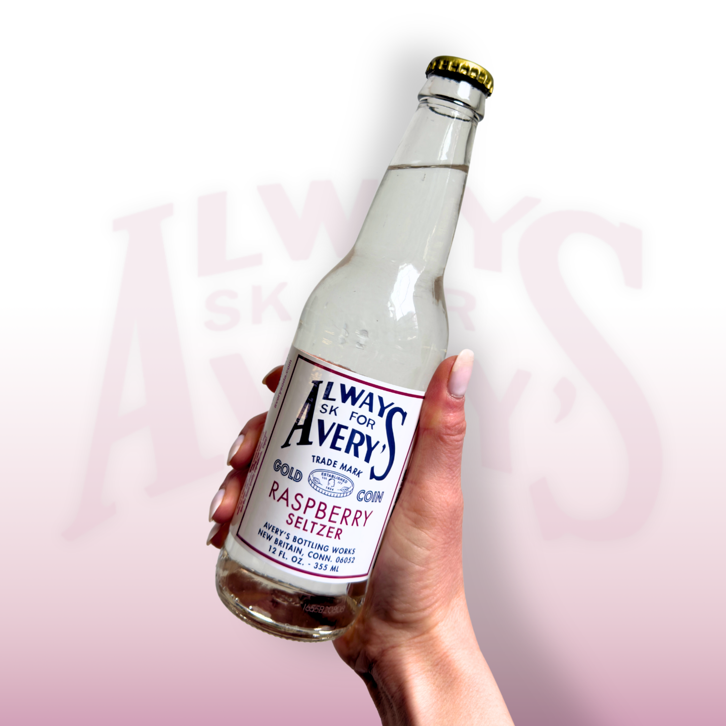 Hand holding a bottle of Avery’s Raspberry Seltzer in glass bottle on pink gradient background