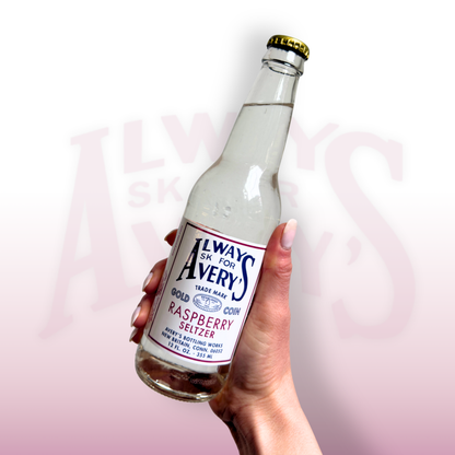 Hand holding a bottle of Avery’s Raspberry Seltzer in glass bottle on pink gradient background
