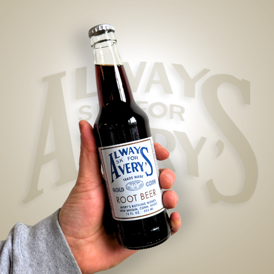Hand holding a bottle of Avery’s Root Beer in glass bottle on brown gradient background