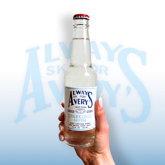Hand holding a bottle of Avery’s Sparkling Seltzer in glass bottle on blue gradient background